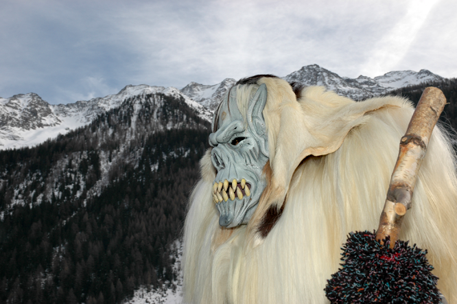 An der Lötschentaler Fasnacht fügt sich ein Tschäggättä mit helllauem Totenkopf in den Horizont der südlichen Bergkette.